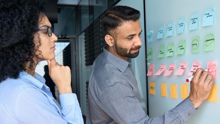 Decorative image of two workers collaborating in a brainstorm using sticky notes.